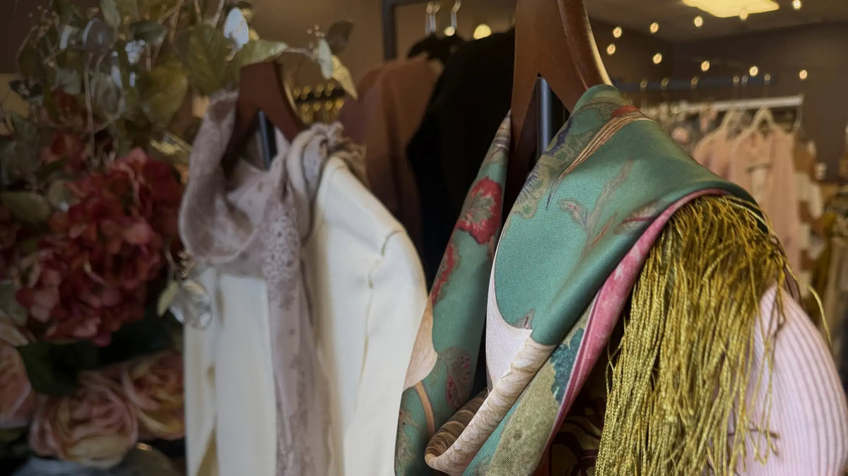 A vibrant green and pink patterned silk scarf with gold fringe hanging on a wooden hanger.